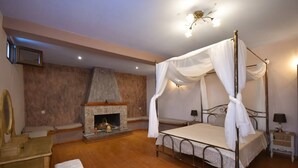 A bedroom with a four-poster bed, a stone fireplace, a wooden chair, and a nightstand with a lamp. - Villa in Malaki in Sea With PlayGround (Malaki)