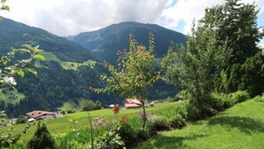 A rural landscape with a house, green fields, and mountains in the background.