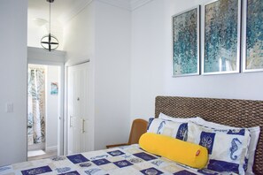 Un dormitorio con una cama, una silla, una puerta y una pared con tres obras de arte enmarcadas.