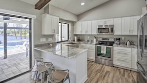 Cozinha moderna com armários brancos, uma ilha grande com pia, eletrodomésticos de aço inoxidável e vista para uma piscina através de uma porta de vidro.