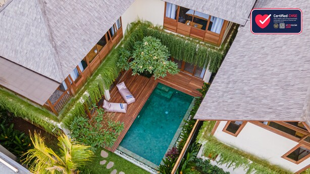 Un área de piscina en la azotea con terraza de madera, sillones de descanso y abundante vegetación.