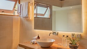 Un baño con tocador de madera, un espejo grande, un lavamanos blanco y un inodoro.