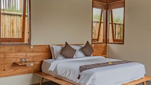 Un dormitorio con estructura de cama de madera, ropa de cama blanca y dos ventanas con marcos de madera.