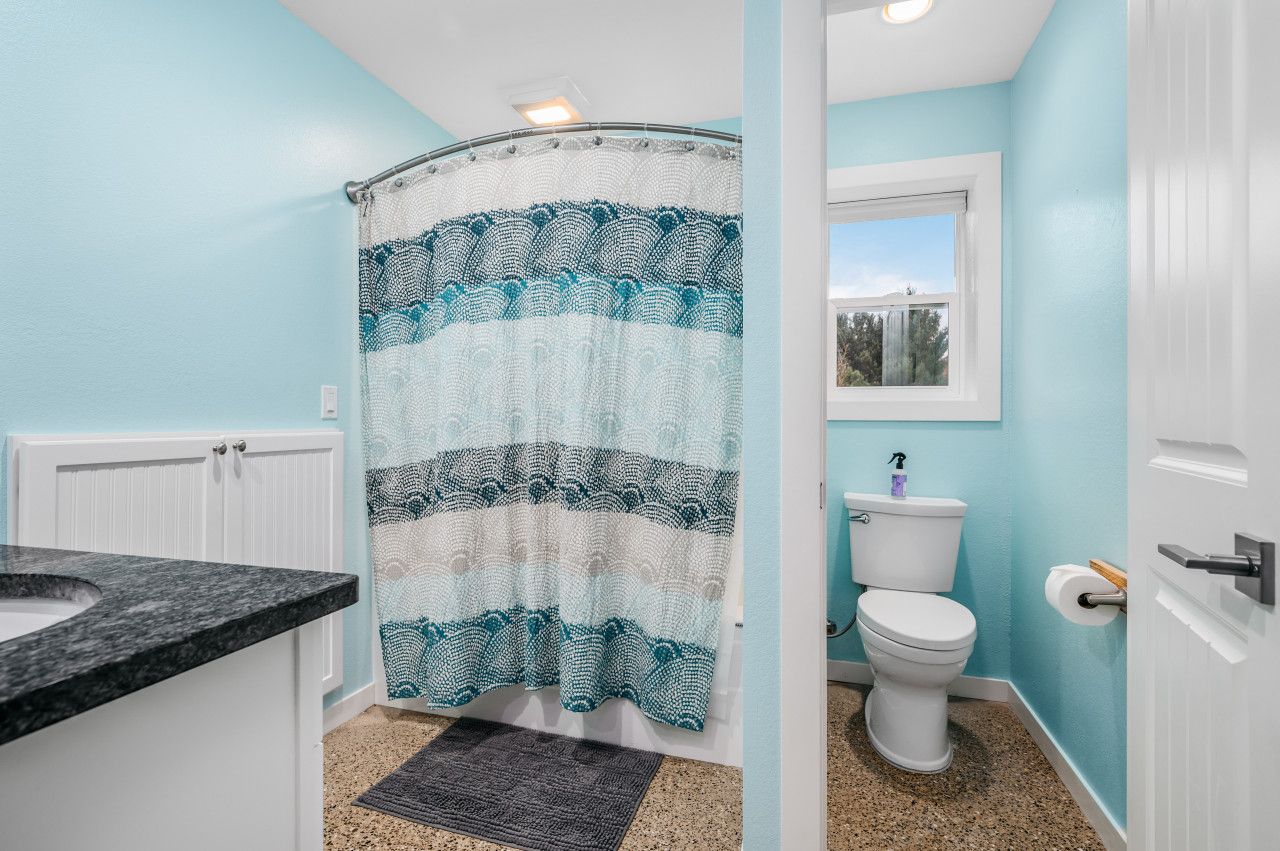 Een badkamer met een gebogen douchegordijn, een toilet, een wastafel en een raam.