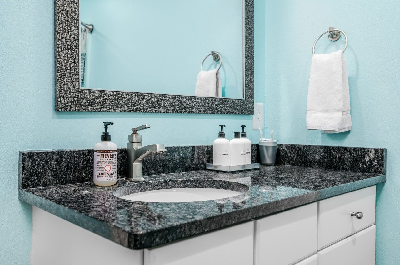 A bathroom with a granite countertop, a white sink, a mirror, and toiletries.