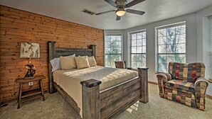 A bedroom with a wooden headboard, a bed with a beige bedspread, a wooden nightstand, a chair, and a ceiling fan. - Charming Hamilton Farmhouse w/ Country Views! (Gustine)