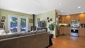 Ein geräumiges Wohnzimmer mit einer großen Couch, einem Fernseher und einem Essbereich mit Holzsärchen und einer Küche im Hintergrund.