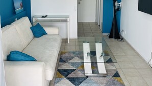 Uma sala de estar moderna com um sofá branco, uma mesa de centro de vidro e uma parede de destaque azul.
