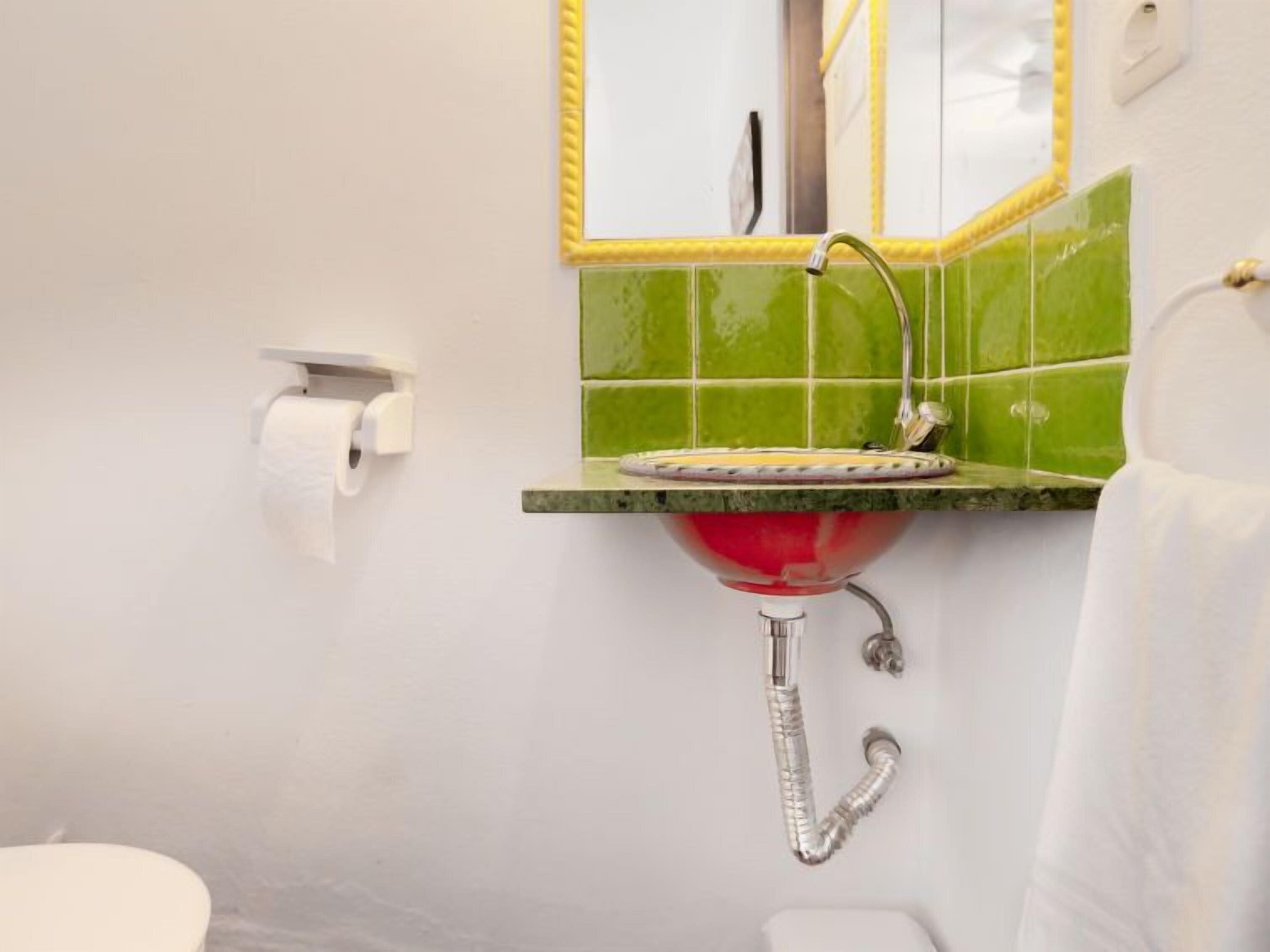 A bathroom with a green tiled wall, a white toilet, a red sink with a silver faucet, and a white towel hanging on the wall.