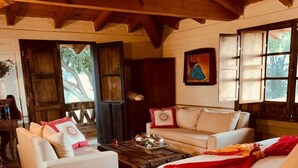 Une pièce chaleureuse avec un canapé blanc, un lit recouvert d’une couverture rouge et un plafond en bois.