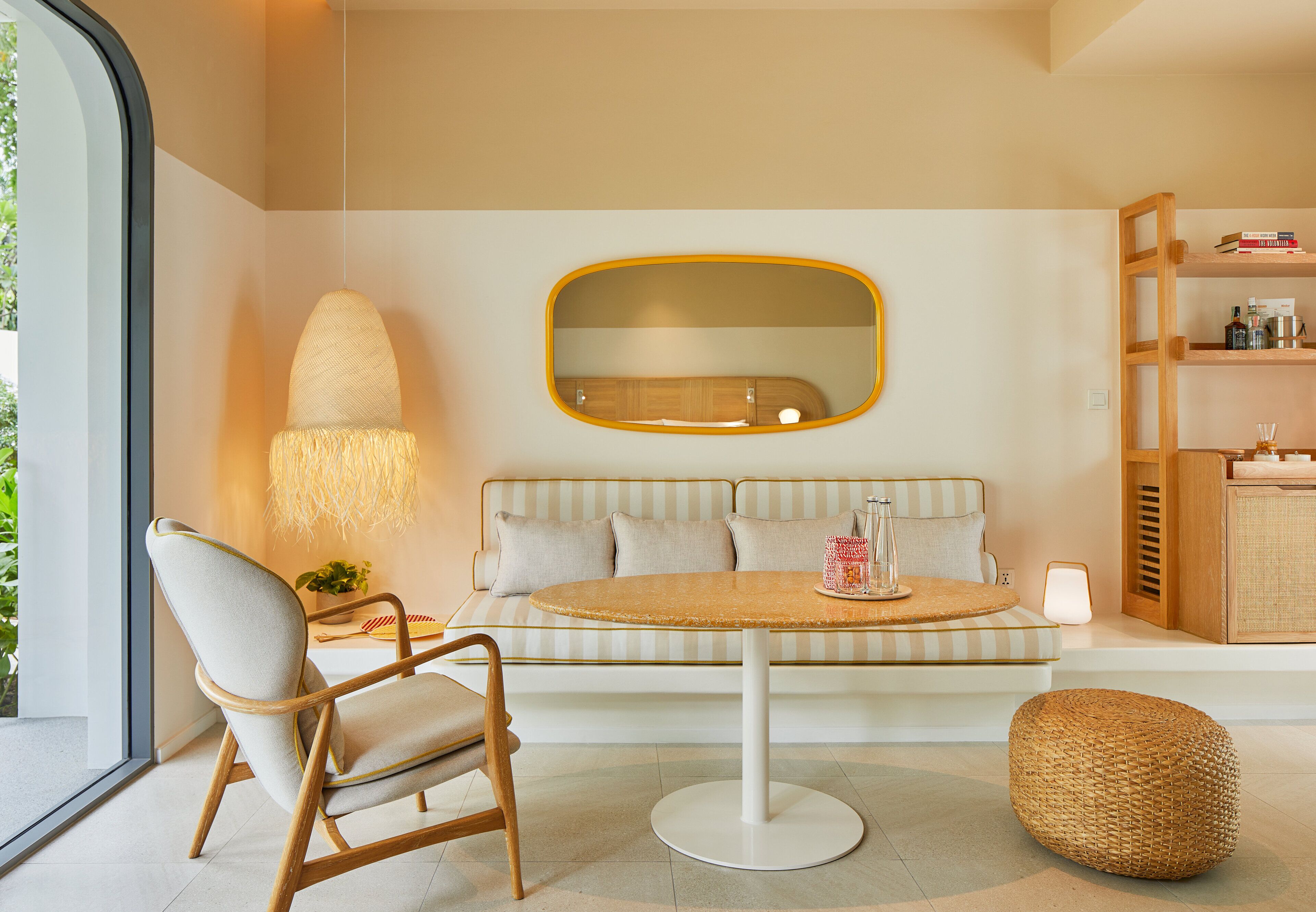 A modern living room with a round table, a sofa, a chair, a large mirror, and a bookshelf.