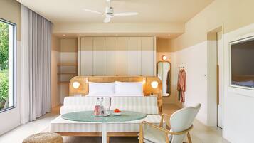 A modern hotel room with a large bed, a round dining table, a chair, a ceiling fan, and a large window.