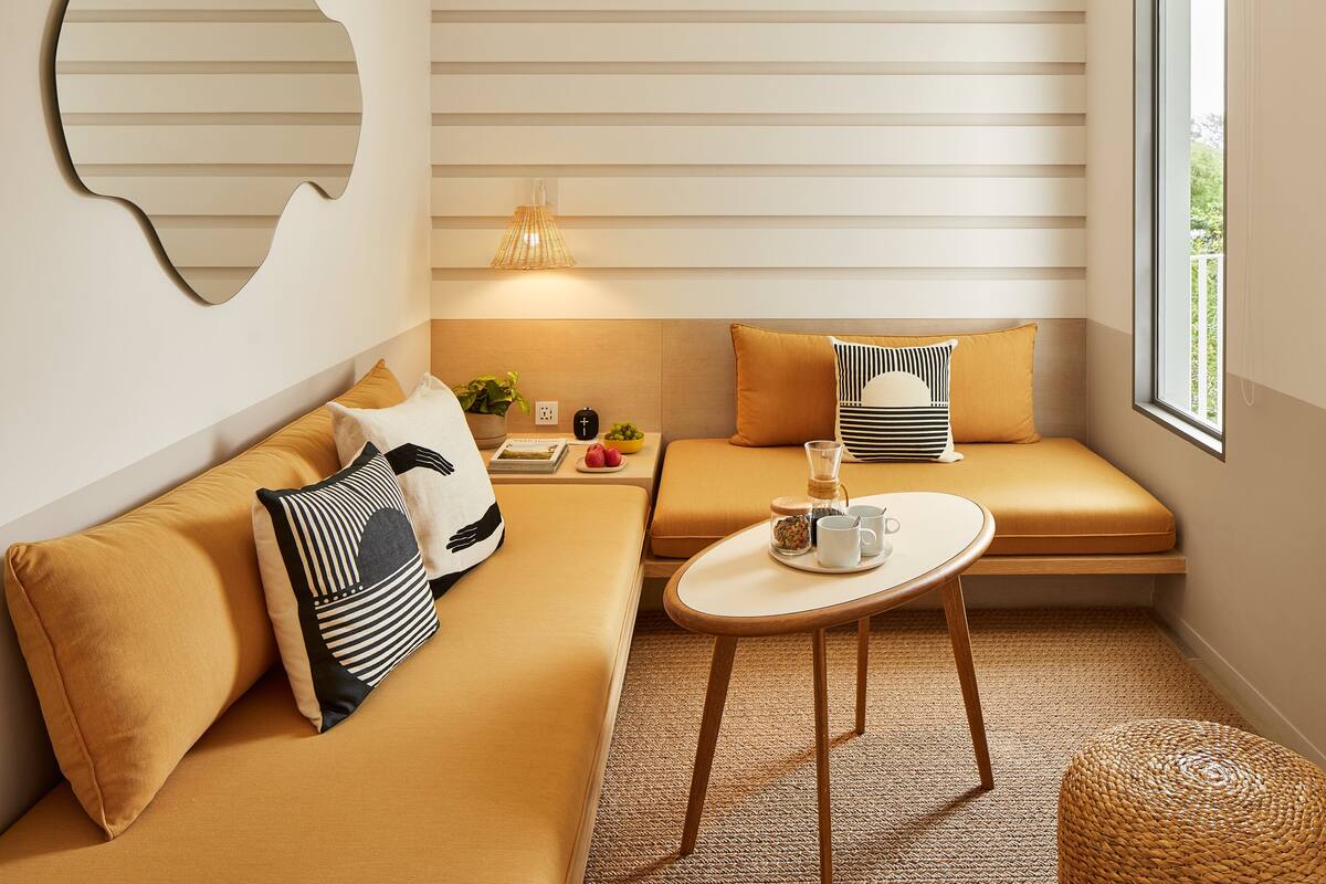 Eine gemütliche Ecke mit einer Couch, einem kleinen Tisch und einem Fenster mit Jalousien.