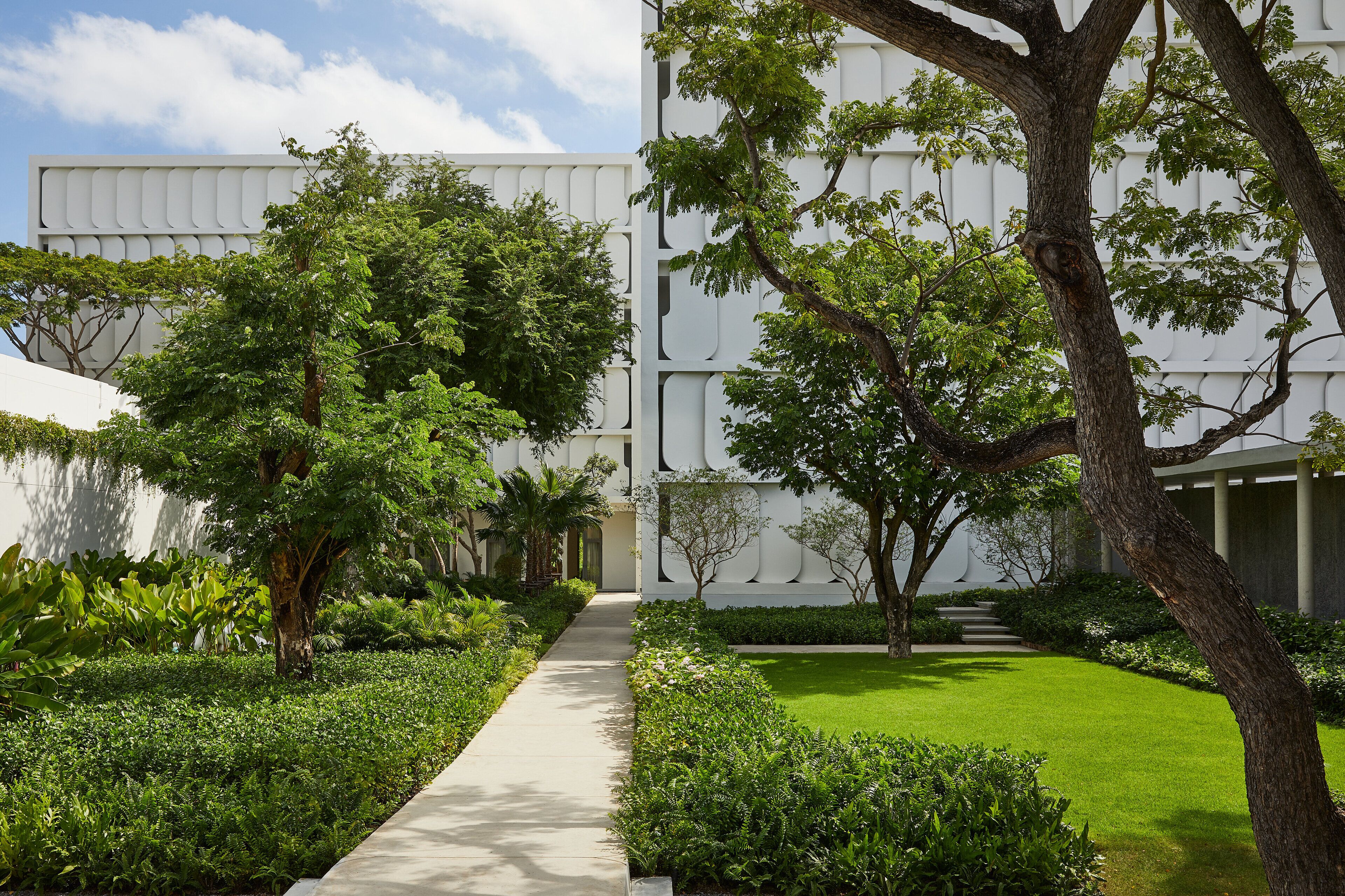 A modern building with a geometric facade, surrounded by lush greenery and a well-maintained lawn.