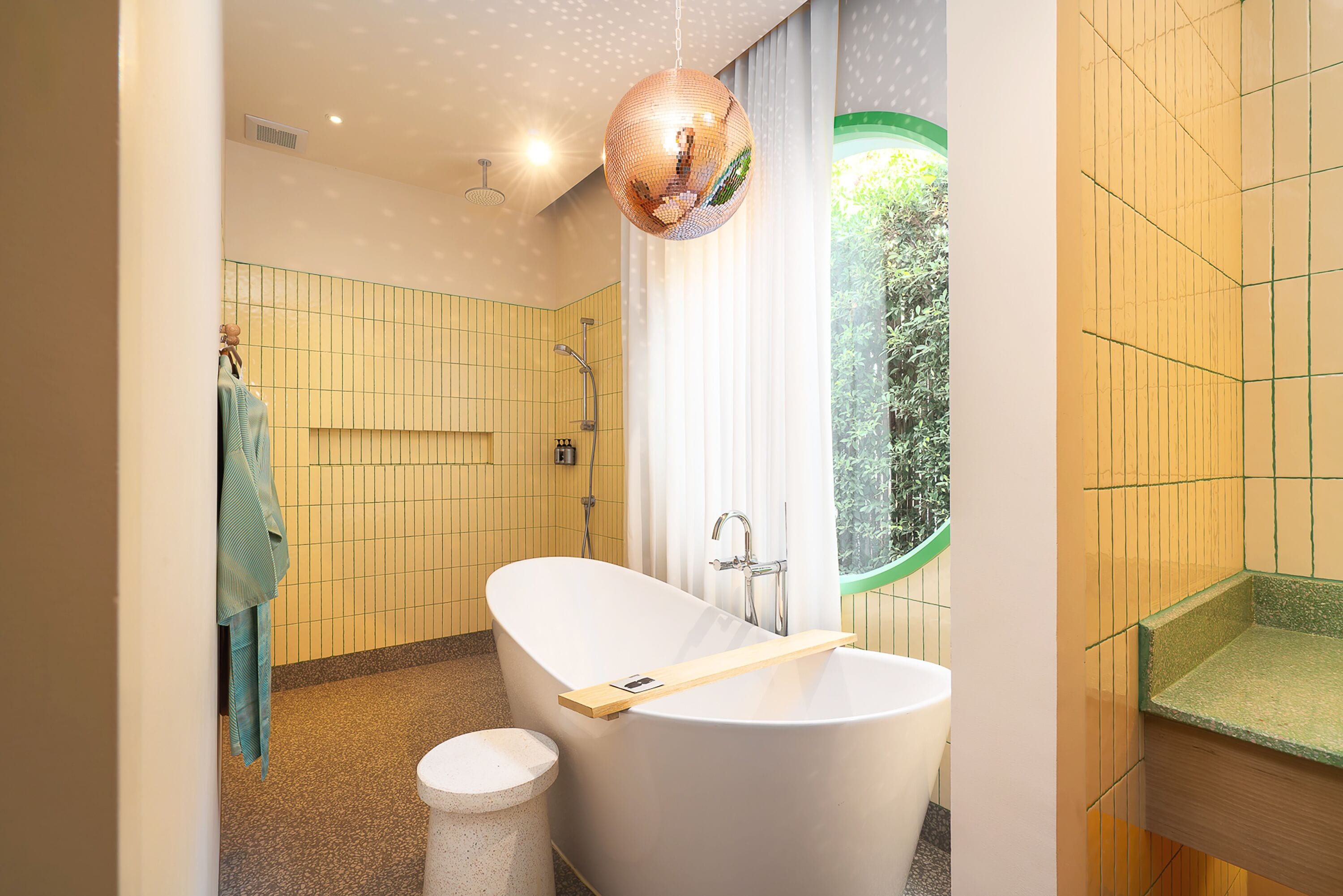 A modern bathroom with a freestanding bathtub, a shower, and a window with a view of greenery.