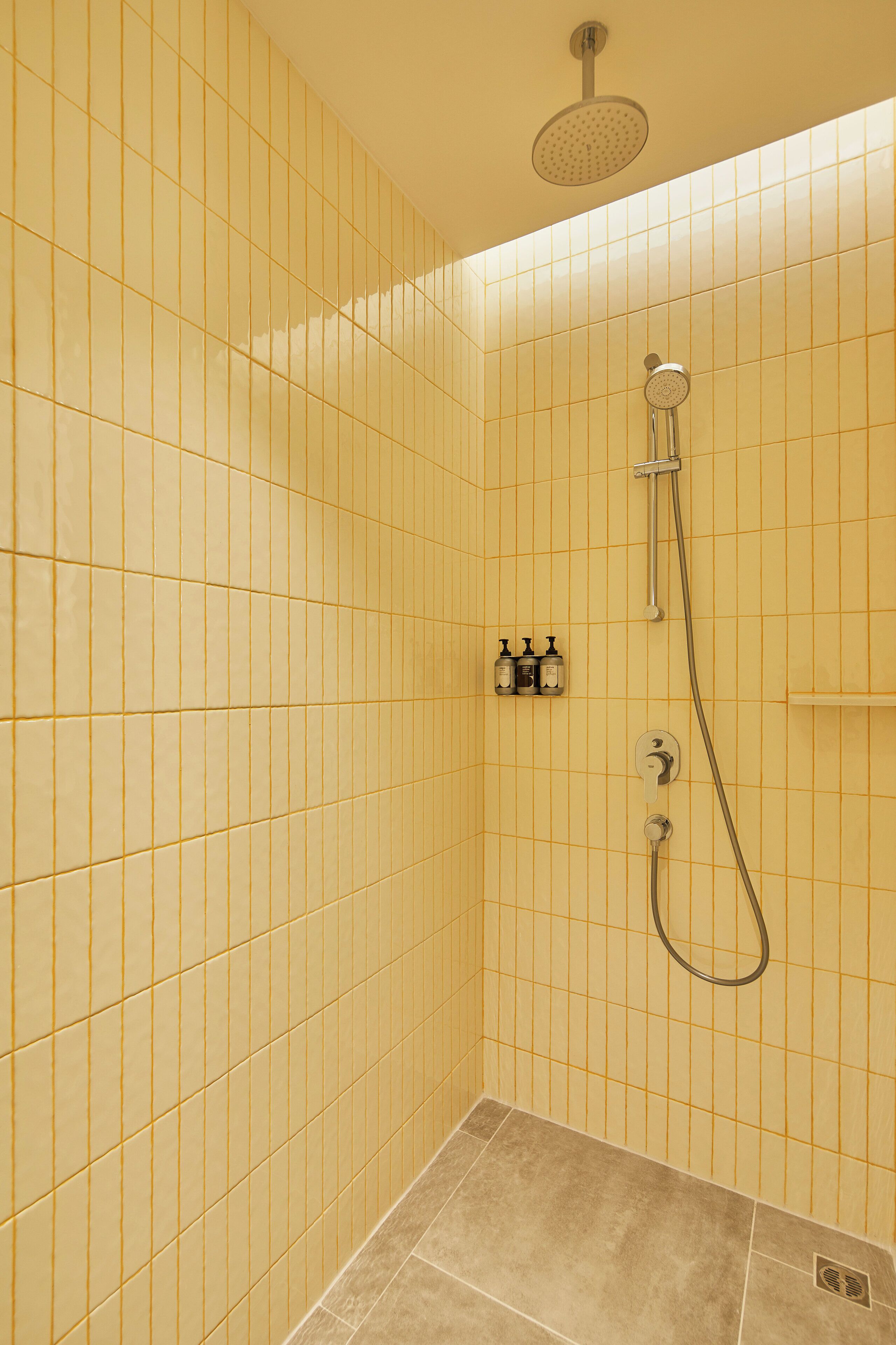 A small, tiled shower room with a handheld showerhead and a wall-mounted faucet.