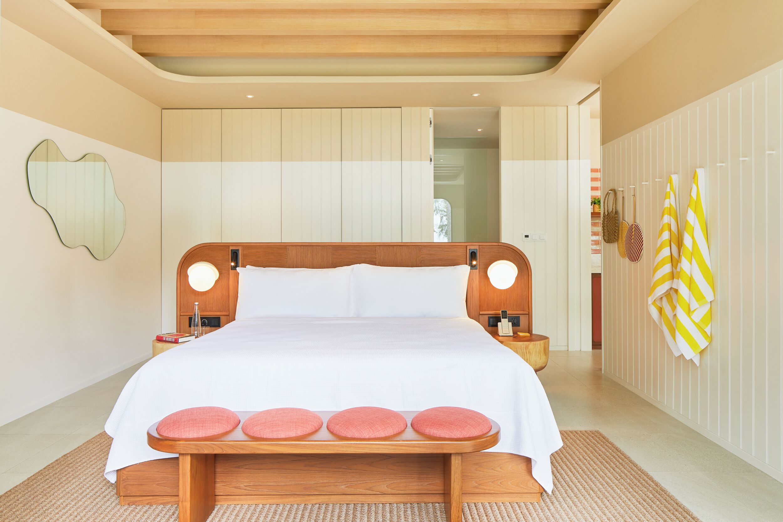 A hotel room with a wooden bed, white bedding, a bedside table, a wall-mounted lamp, and a striped towel on the wall.