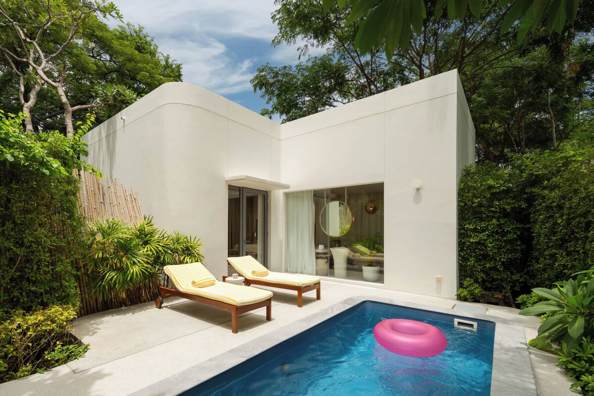 Ein modernes Haus mit Schwimmbecken, zwei Liegestühlen und üppiger Bepflanzung.