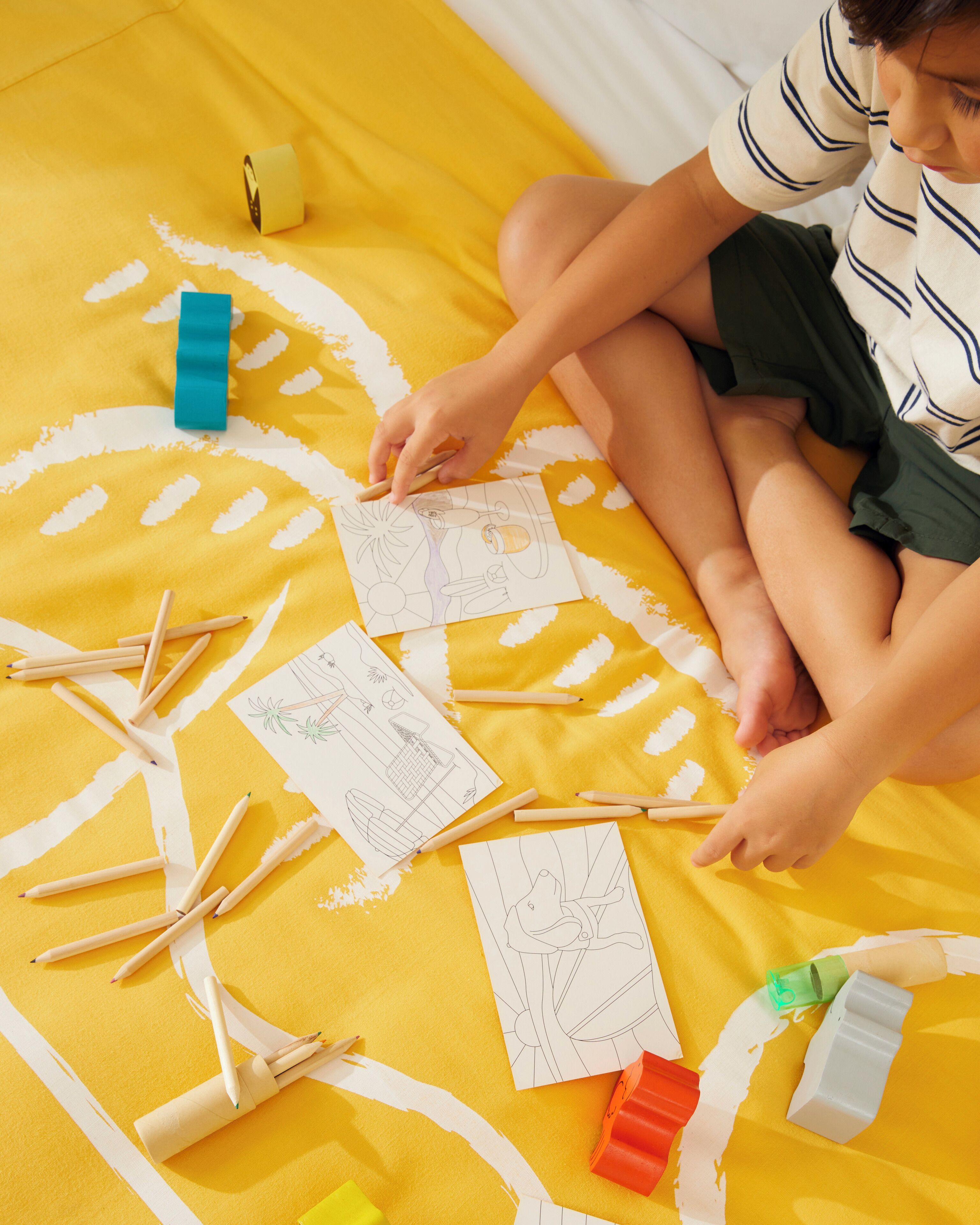 A child drawing on a yellow surface with various art supplies.