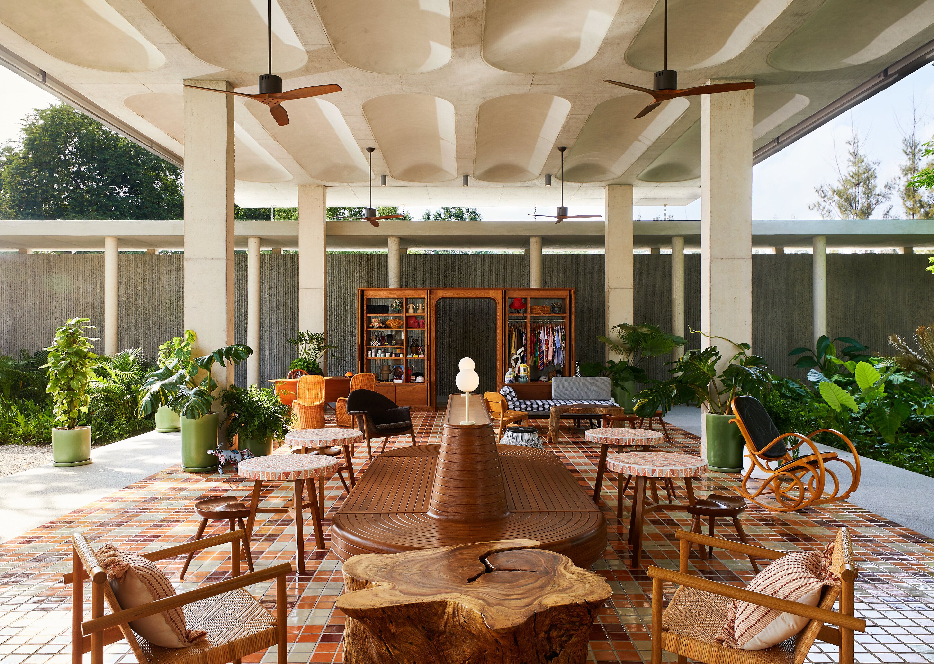 An outdoor patio with a central wooden table surrounded by chairs, a bookshelf, and potted plants.