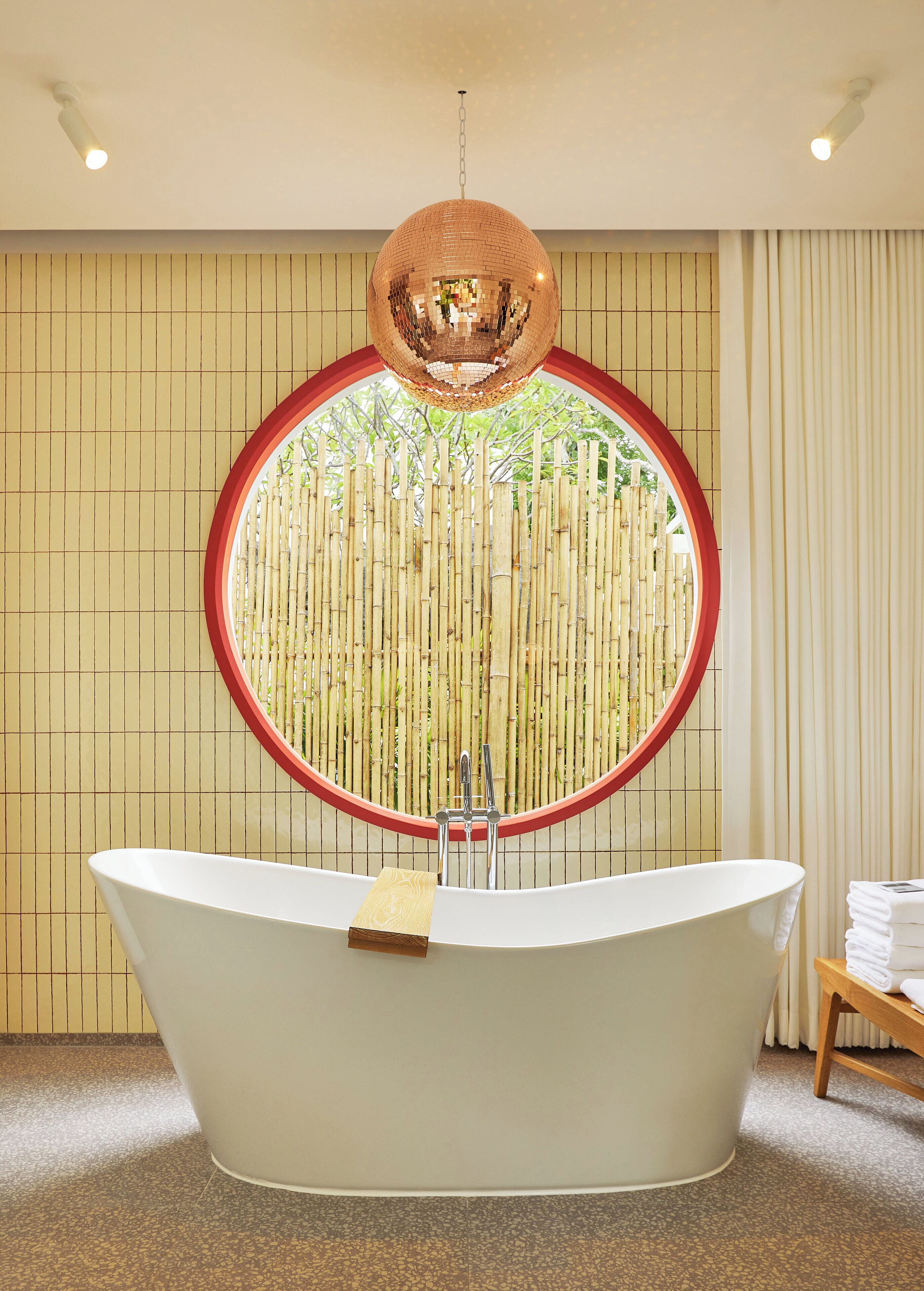 A modern bathroom with a freestanding bathtub, a circular mirror, and a hanging disco ball.