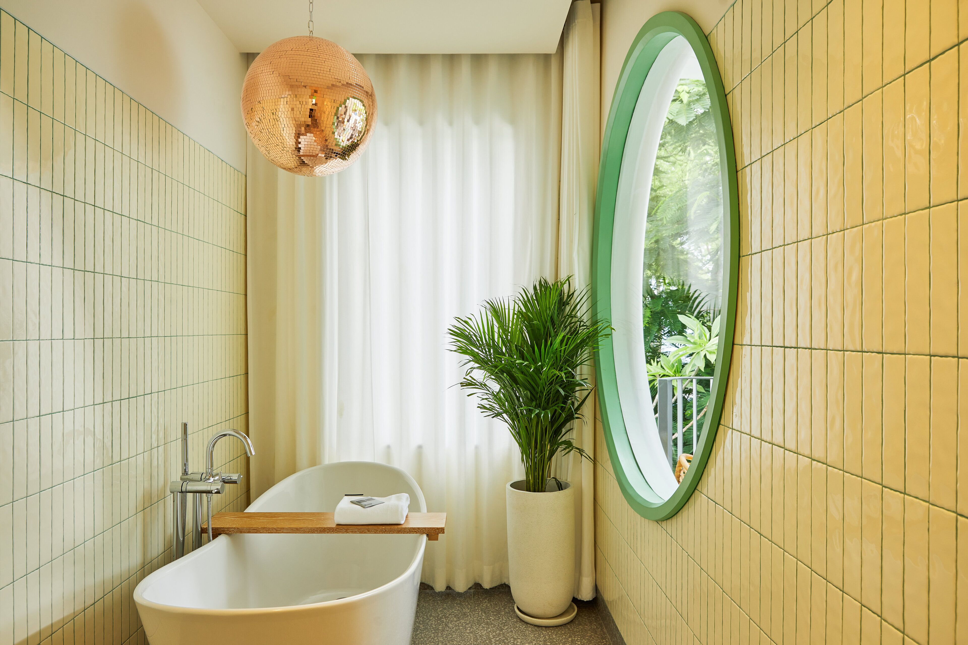 A bathroom with a freestanding bathtub, a large mirror, and a potted plant.