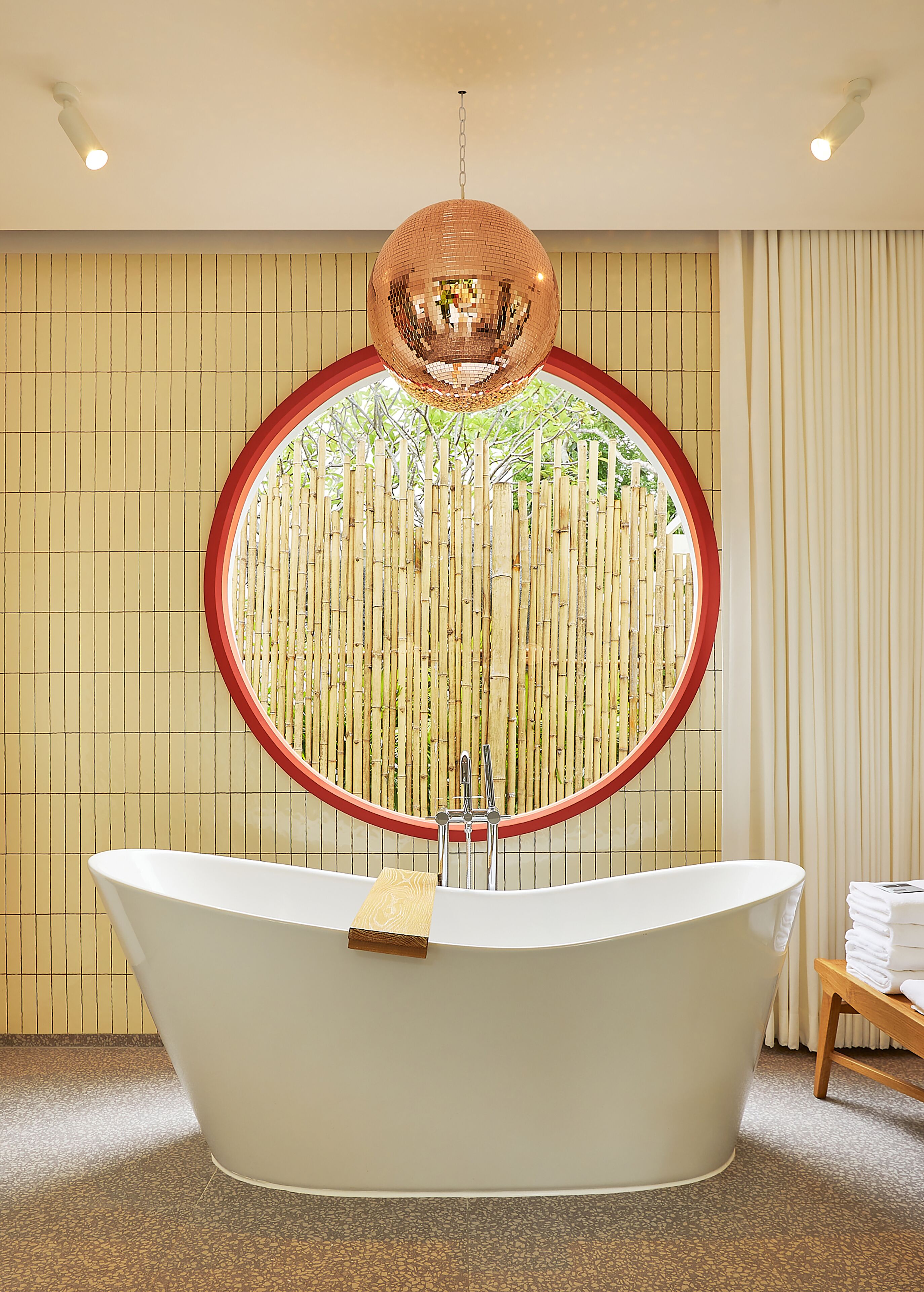 A modern bathroom with a freestanding bathtub, a circular mirror, and a hanging disco ball.