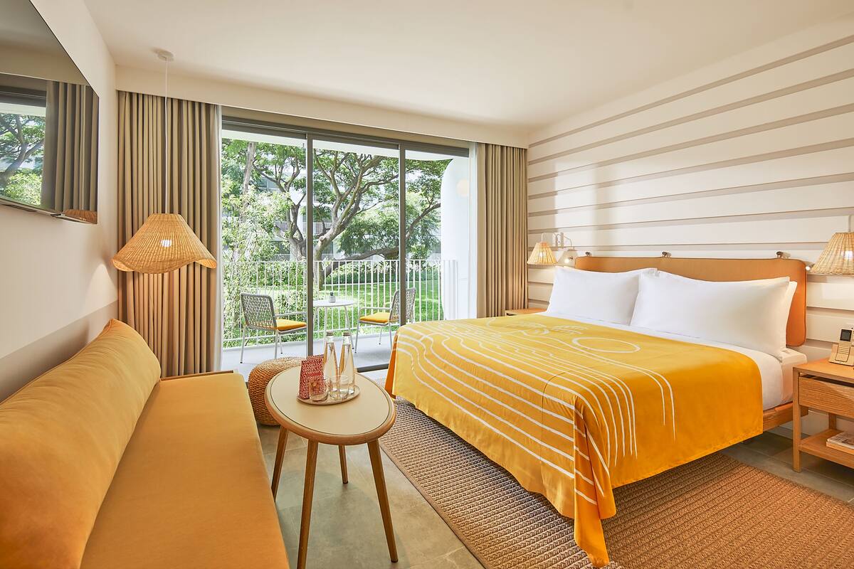Ein Hotelzimmer mit einem großen Bett, einem Schlafsofa, einem kleinen Tisch mit einer Lampe und Blick ins Freie.