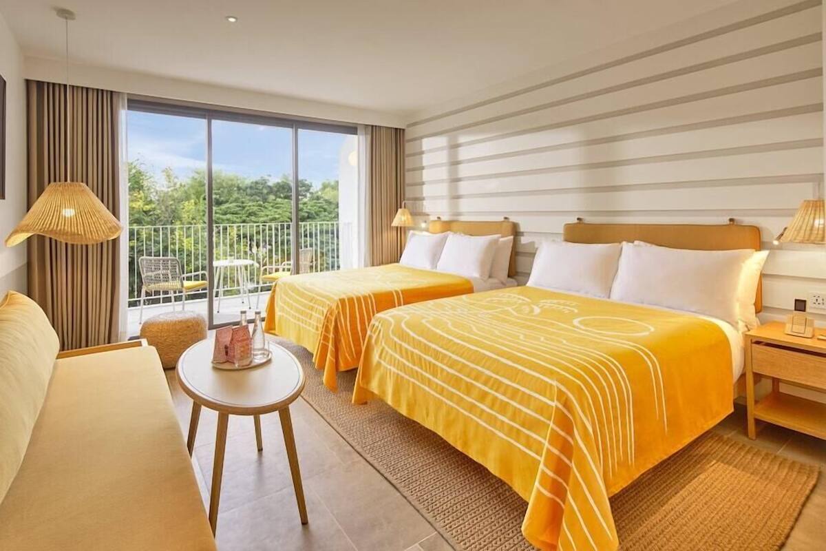 Ein Hotelzimmer mit zwei Betten, einem Balkon, einer Couch, einem kleinen Tisch und einem Nachttisch.