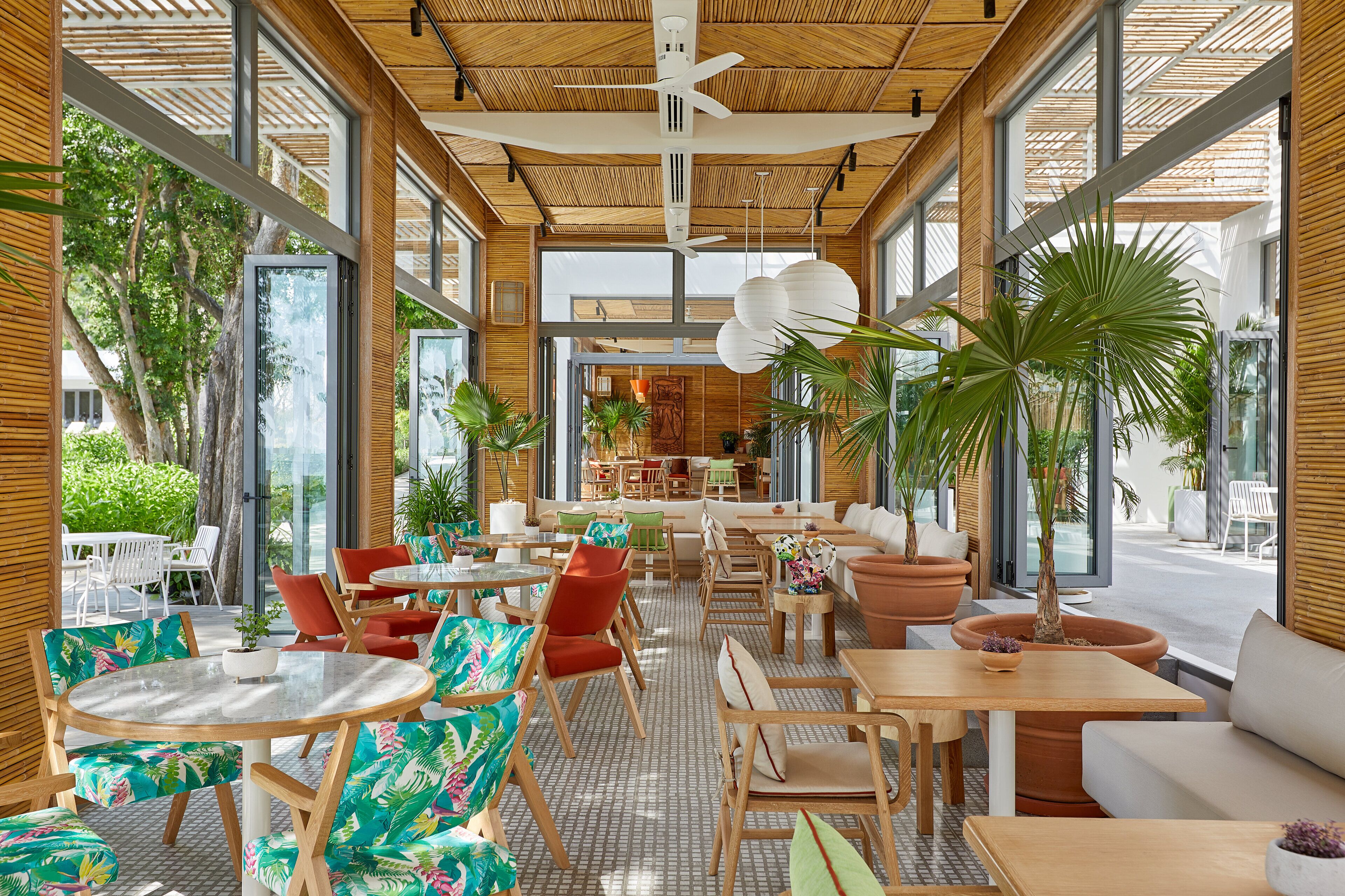 A spacious indoor area with wooden flooring, large windows, and a variety of seating arrangements including tables and chairs.
