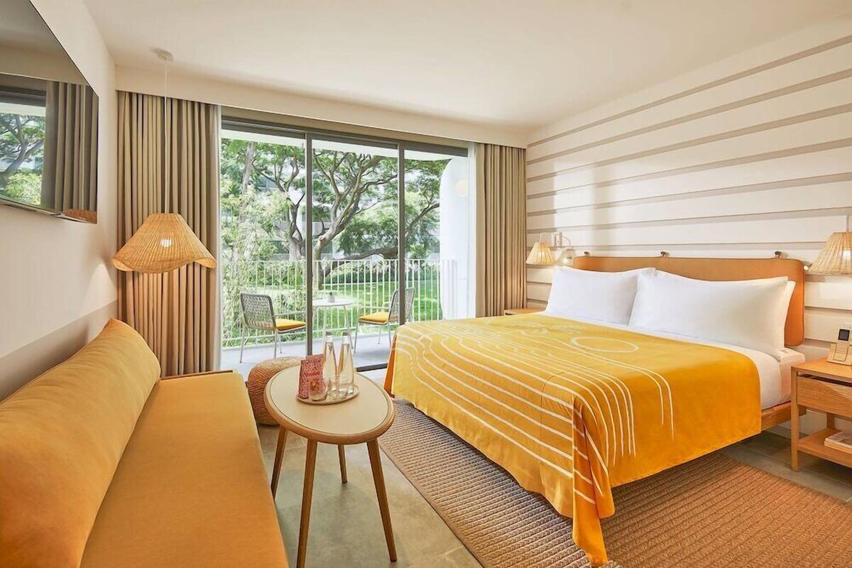 Ein Hotelzimmer mit einem Bett, einer Couch, einem kleinen Tisch, einer Lampe und Blick auf Grünfläche.