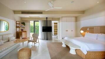 A modern hotel room with a large bed, a sofa, a TV, and a balcony with a view of greenery.