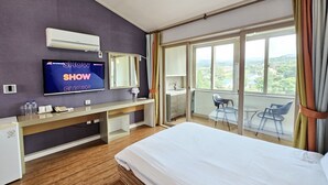 A hotel room with a large bed, a TV mounted on the wall, a desk with a chair, and a balcony with a view. - Haemil Resort (Jeju City)