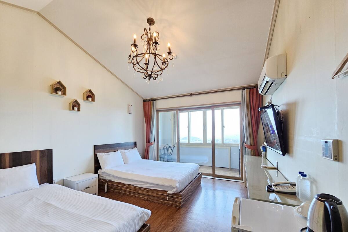 A hotel room with two beds, a chandelier, a TV, and a balcony with a view.