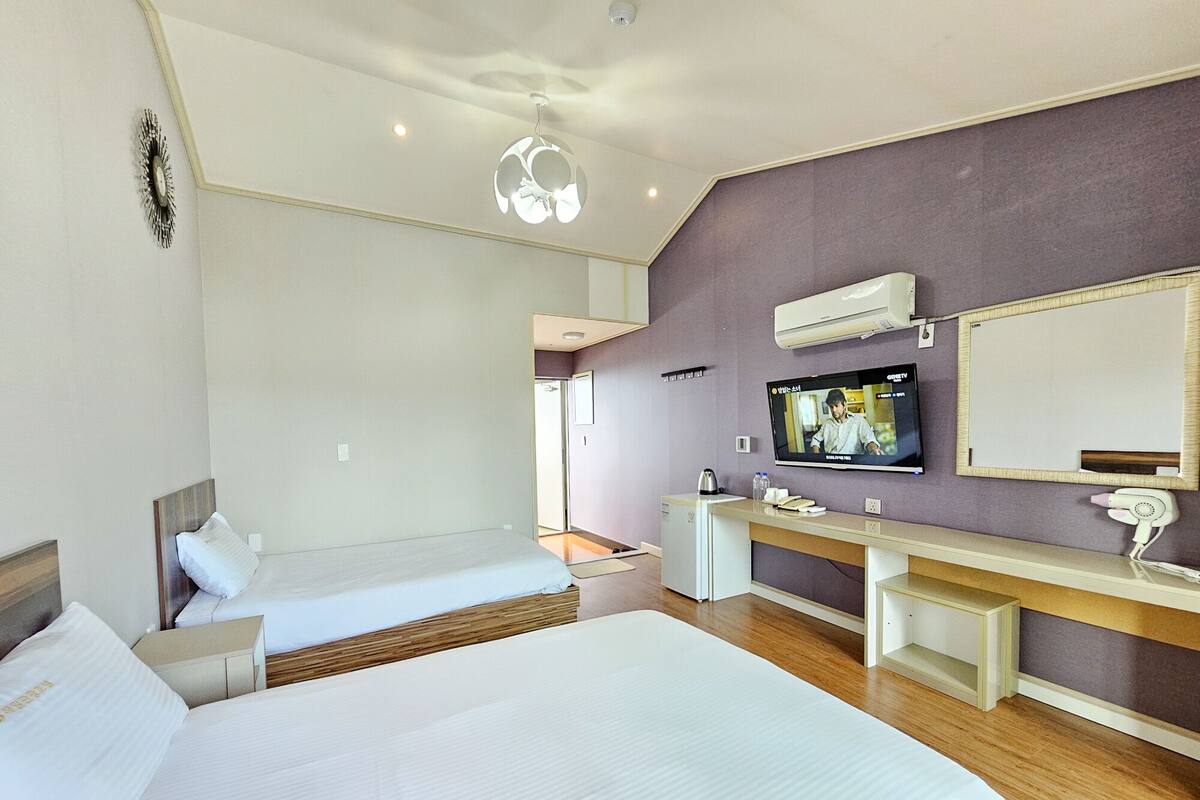 A hotel room with two beds, a TV, a desk with a mirror, and a small kitchenette.