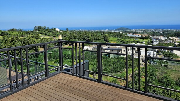 A wooden deck with a metal railing overlooking a coastal landscape with buildings and greenery. - Haemil Resort (Jeju City)