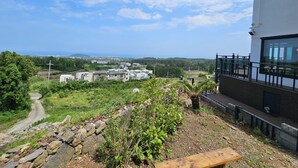 A view of a modern building with a balcony overlooking a rocky garden and a path leading to a distant town. - Haemil Resort (Jeju City)