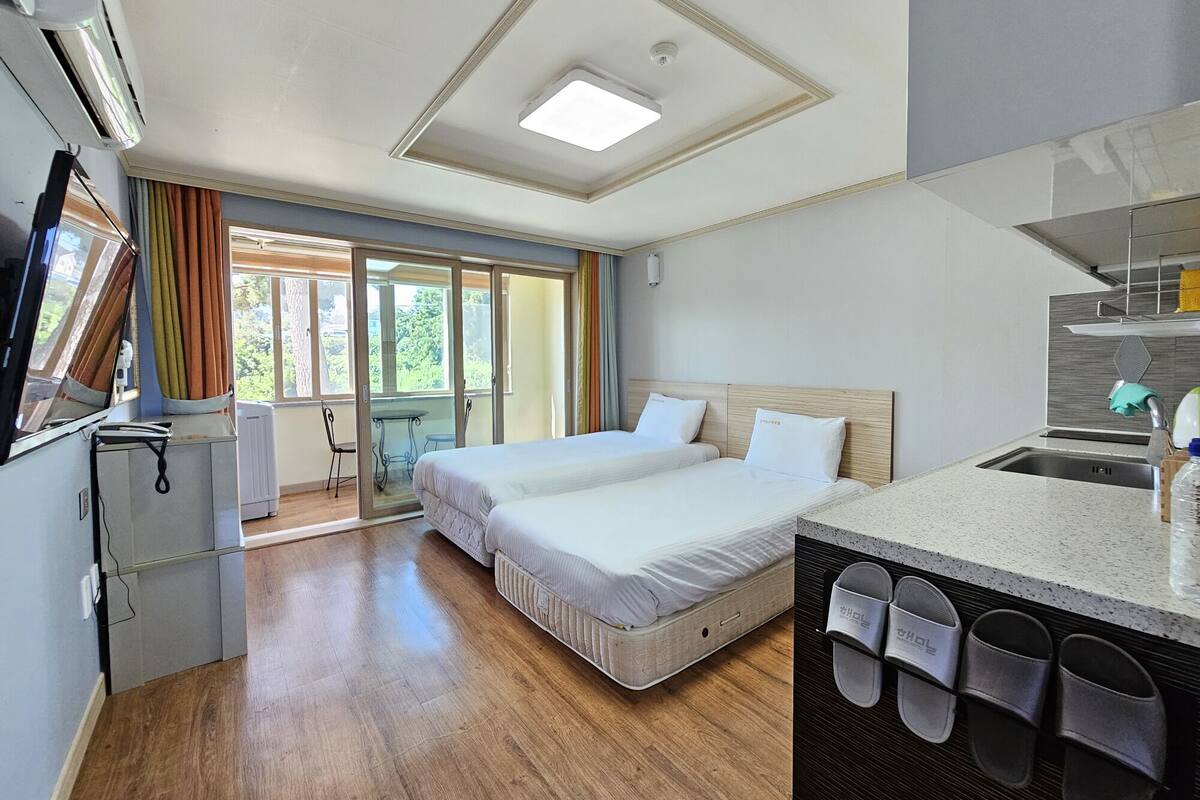 A hotel room with a bed, a small kitchenette, a bathroom, and a sliding glass door to a balcony.