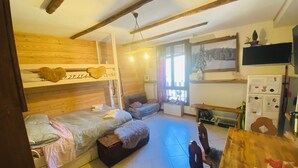 A cozy room with a bunk bed, a small table, and a chair. There is a window with blinds, a wall-mounted shelf, and a refrigerator. - ❤️🏔 The Lantern in the Mountains ❤️🏔 (Pragelato-Ruà TO)