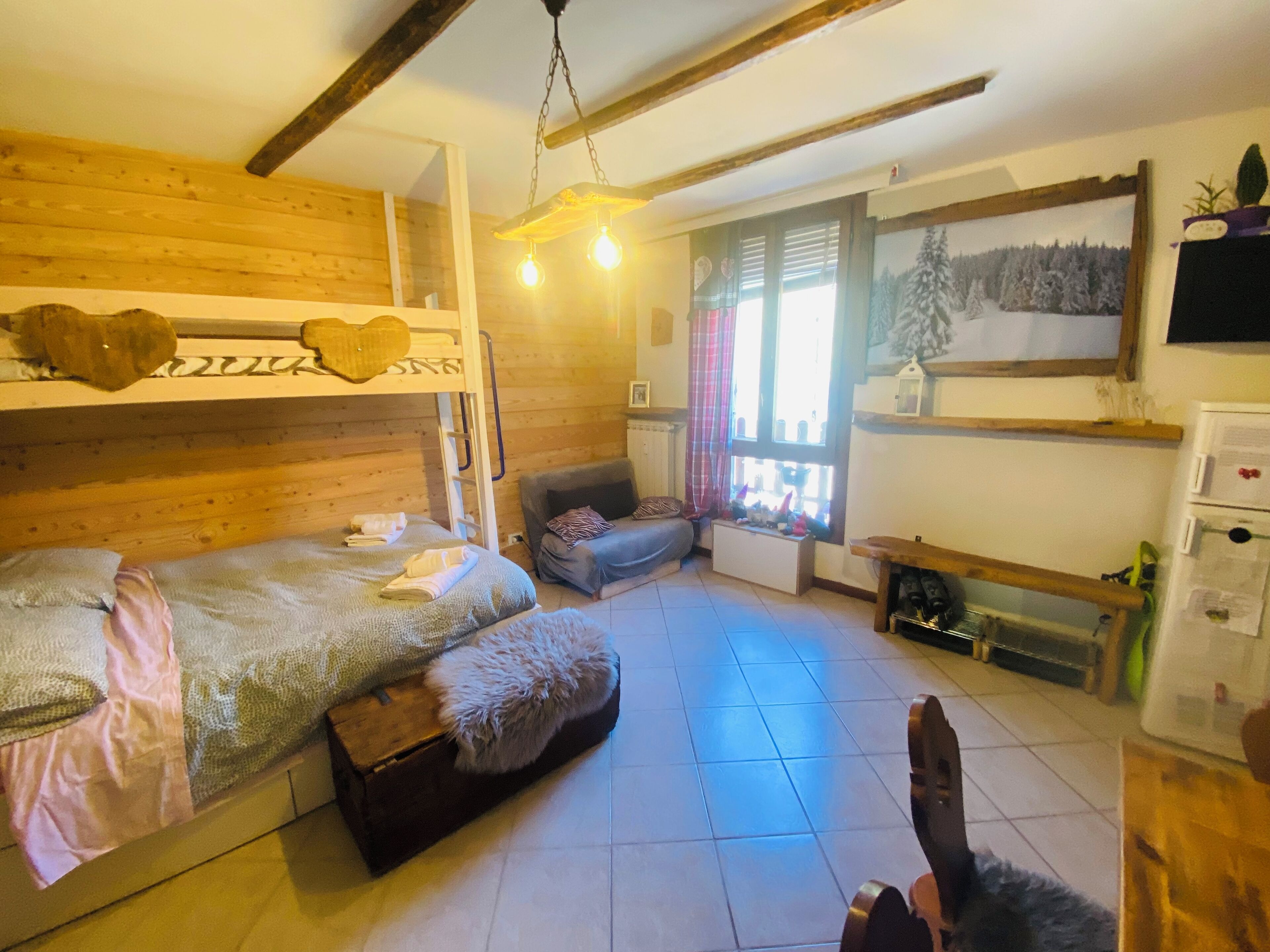 A cozy room with bunk beds, a sofa, a small table, and a window with a view of trees.
