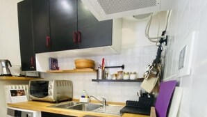 A compact kitchen with a black induction cooktop, a built-in oven, a microwave, and a sink. There are wooden cabinets above the counter and a hanging rack with bags. - ❤️🏔 The Lantern in the Mountains ❤️🏔 (Pragelato-Ruà TO)