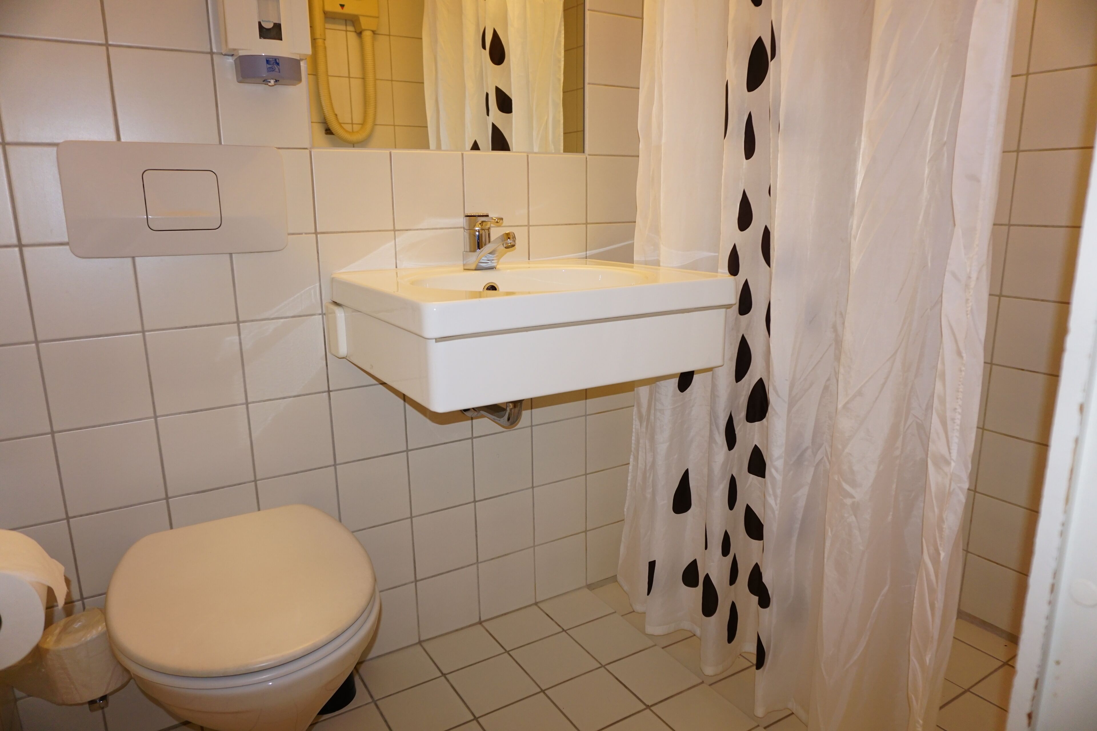 Un baño con inodoro, lavamanos y cortina de ducha.