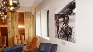 A modern lounge area with leather sofas, a wooden accent wall, and a vintage airplane photo. - Verdde Hotel Lakselv (Porsanger)