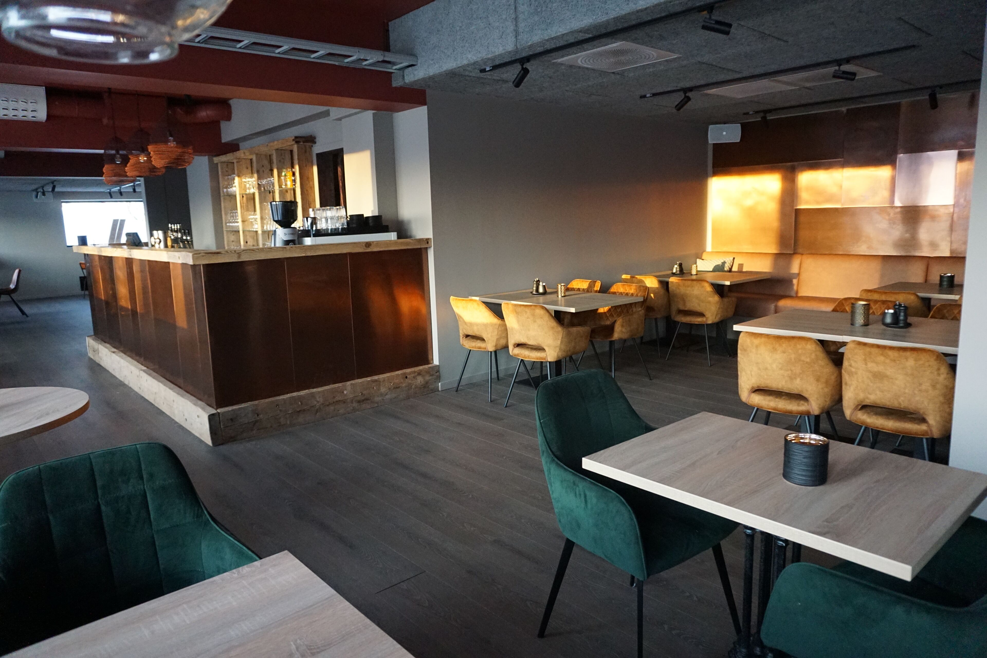 A modern restaurant with a central bar, multiple dining tables, and green upholstered chairs.