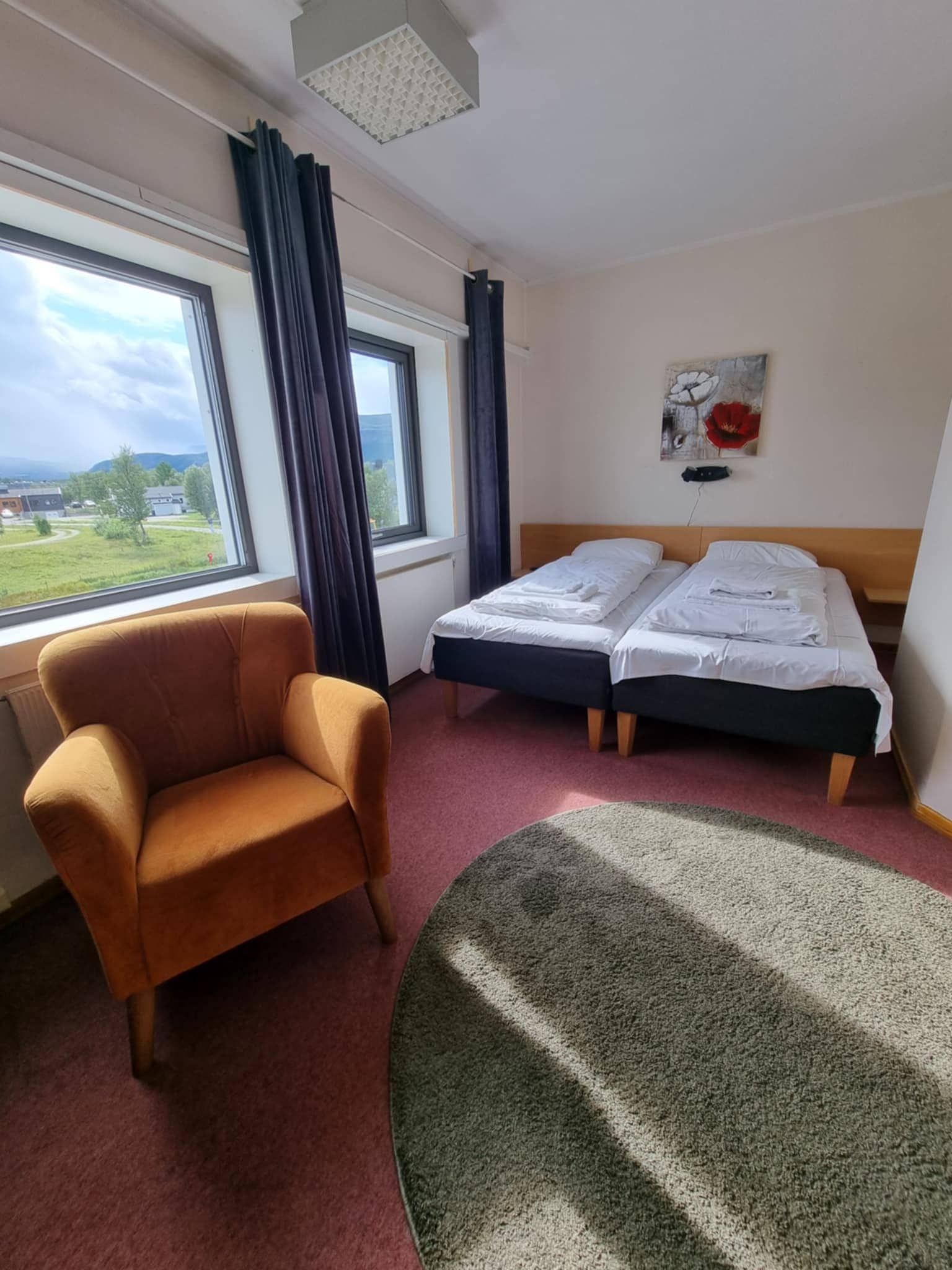 A hotel room with a single bed, a chair, a painting, and a view of the outdoors.