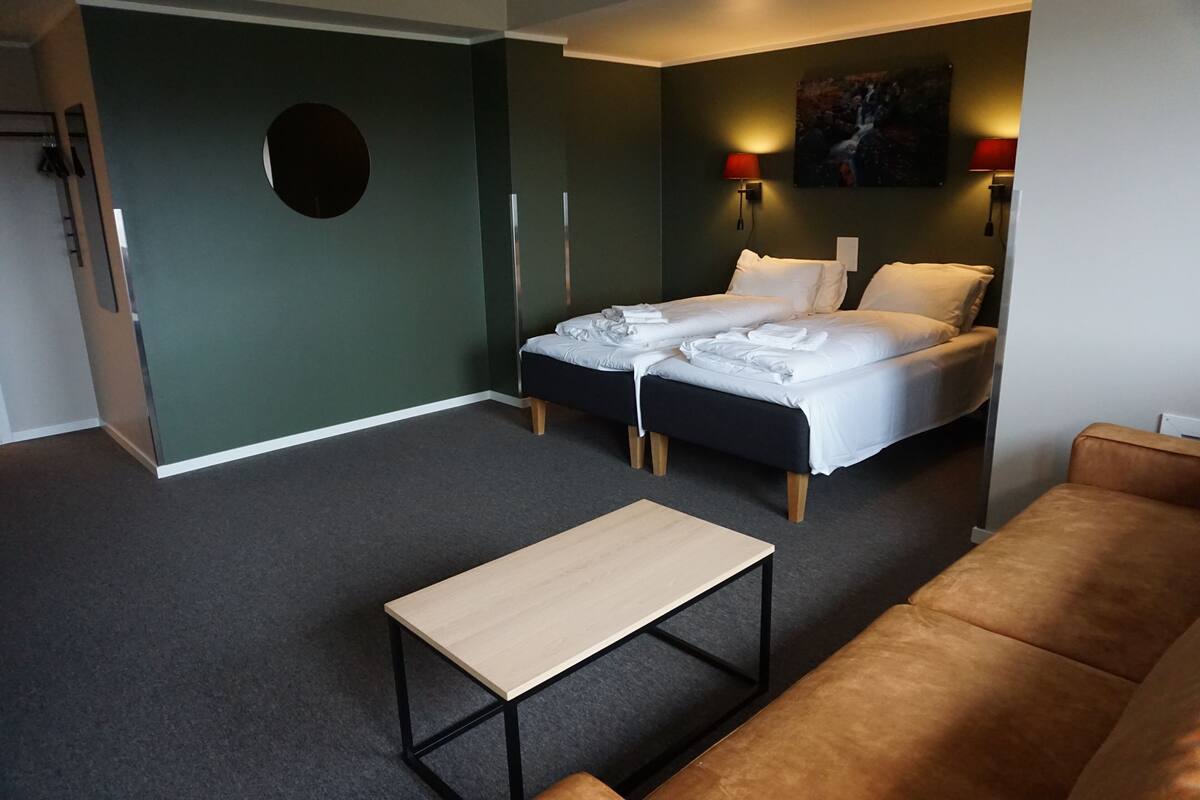 A hotel room with two beds, a sofa, a small table, and a painting on the wall.