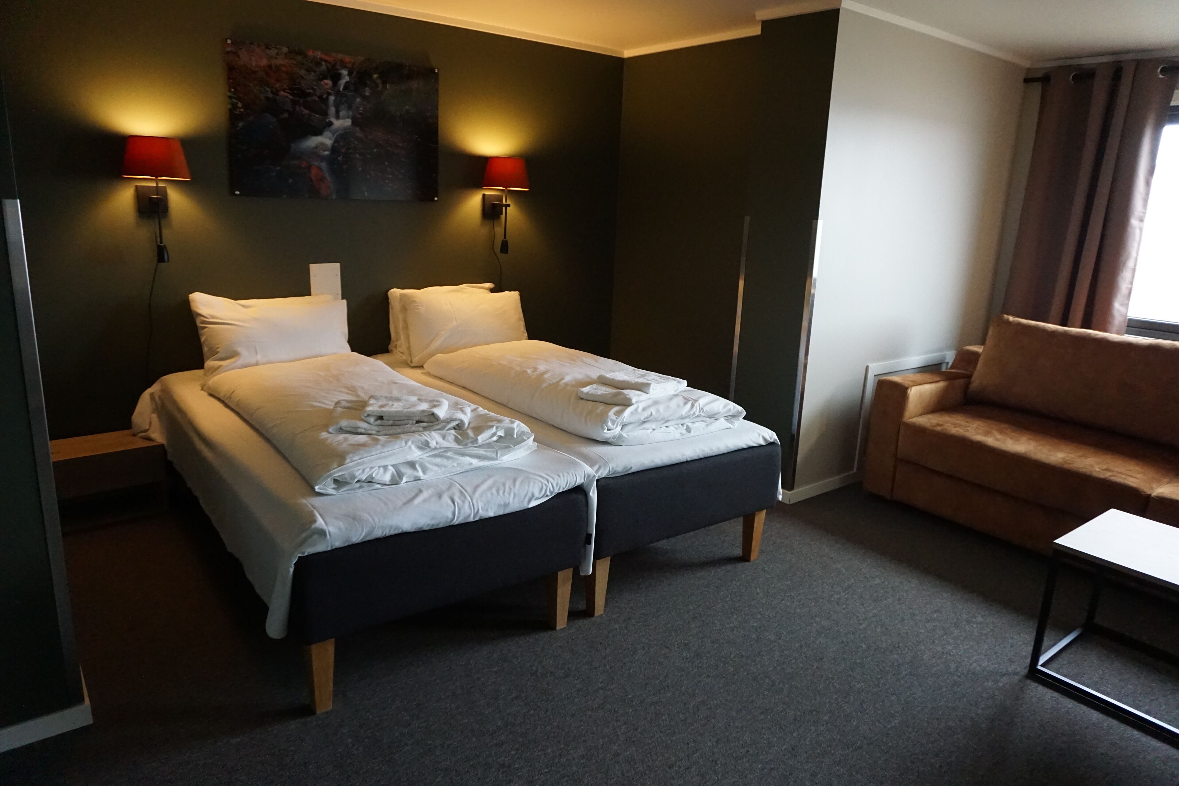 Ett hotellrum med två sängar, en soffa, ett litet bord och två vägglampor.