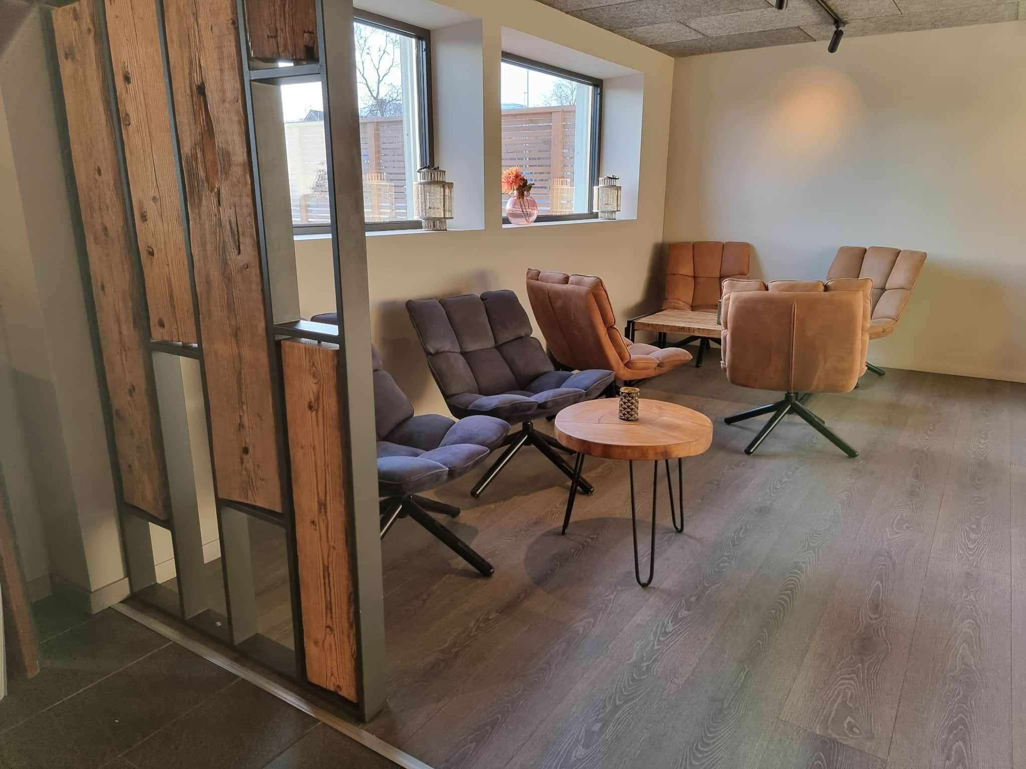 Un interior moderno con suelo de madera, una pared divisoria de vidrio y una disposición de asientos con sofás y sillones.