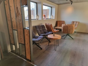 Un intérieur moderne avec un plancher en bois, une cloison en verre et différents types de sièges, notamment des canapés et des fauteuils.