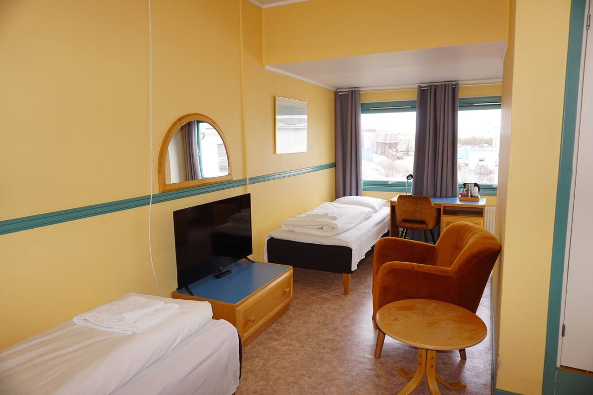 A hotel room with two beds, a TV, a desk, a chair, and a window with curtains.